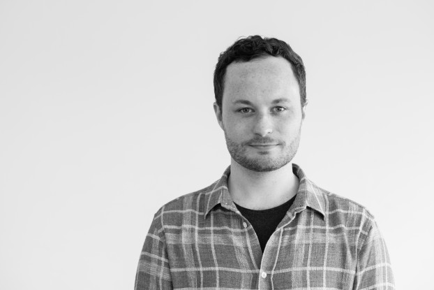 Black and white picture of Aaron Szczerba, positioned off-center and looking at the camera